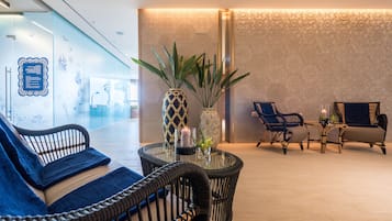 Un hall d’entrée avec un mur en verre, un canapé bleu, une table ronde avec une bougie et deux chaises.
