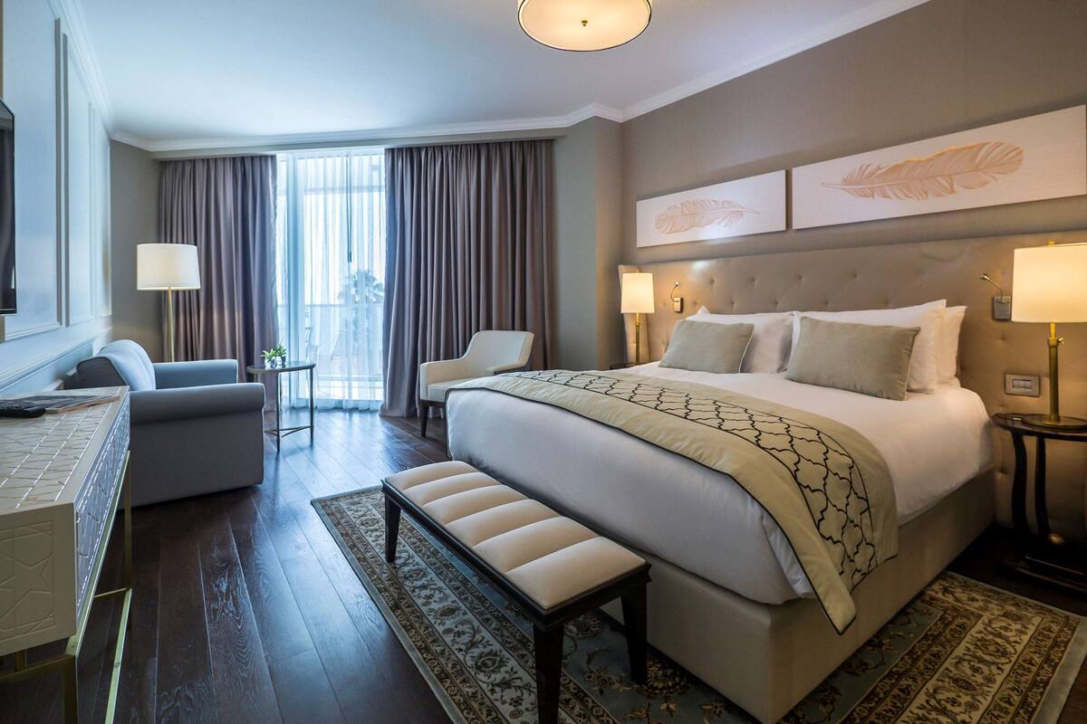 A hotel room with a large bed, a desk with a chair, a sofa, and a view of the outdoors.