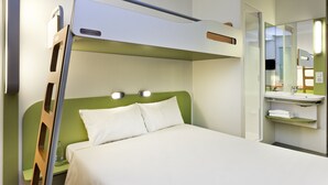 A bunk bed with a ladder, a bedside table with a bottle, a green headboard, and a mirror above a sink.