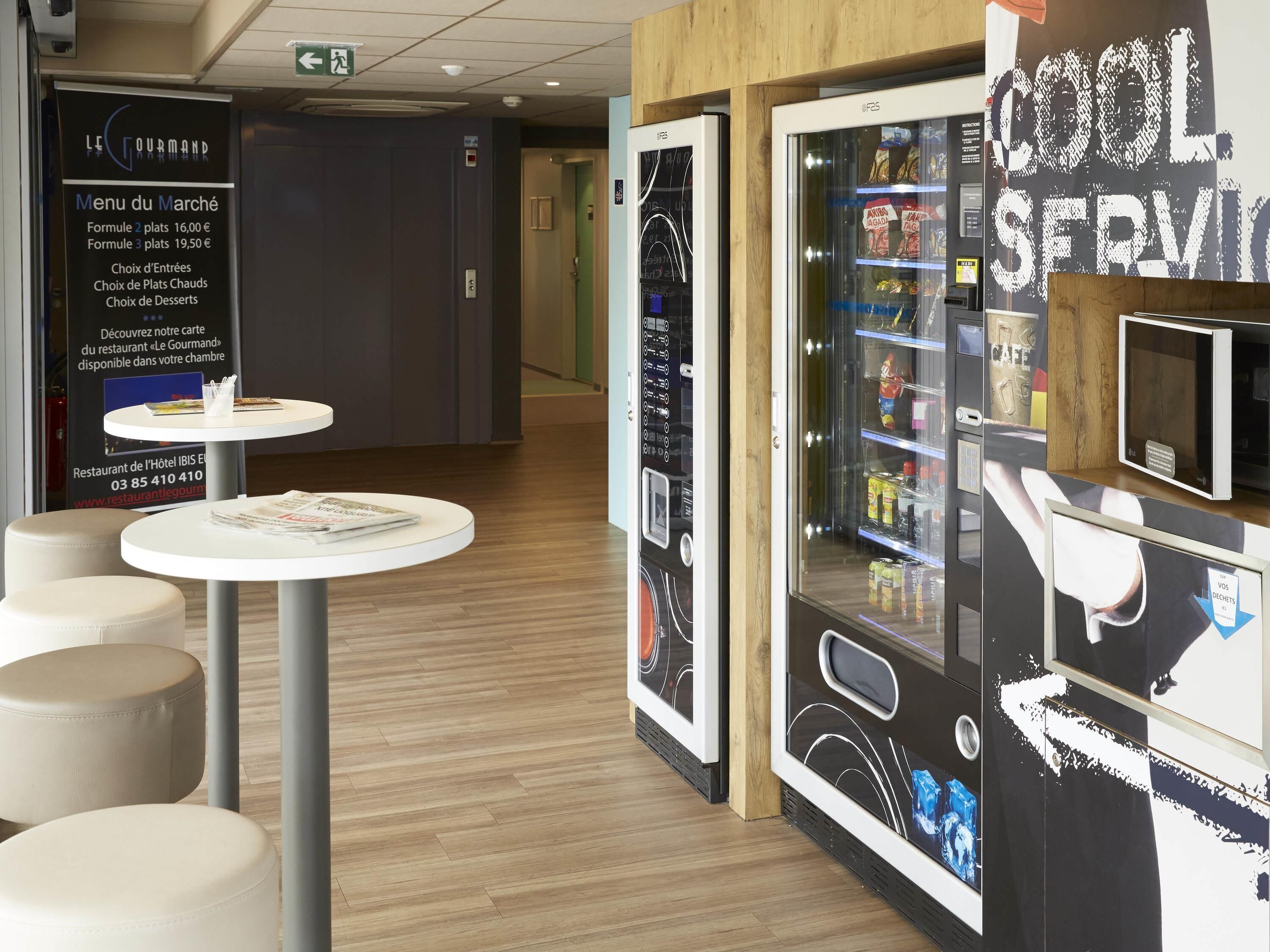 A hotel lobby with a vending machine, a menu board, and seating areas.