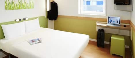 Habitación de hotel con cama, escritorio con computadora, televisor, ventana y espejo adosado a la pared.