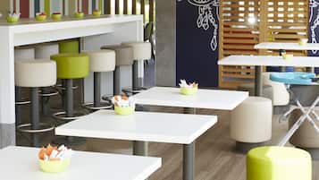 A modern restaurant with white tables and green stools, a TV on the wall, and decorative panels.