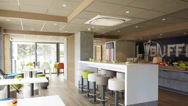 A modern cafe with a central bar area, high stools, and tables with bowls of food. - ibis budget Chalon Sur Saone Nord (Chalon-sur-Saone)