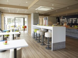 Un café moderno con una barra central, taburetes altos y mesas con fuentes de comida.