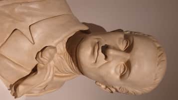 Escultura de una persona con rostro detallado y una prenda con drapeado.