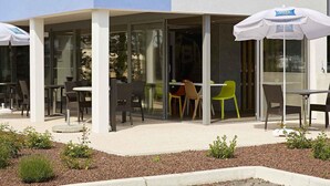 An outdoor seating area with tables and chairs, umbrellas, and a building facade in the background. - ibis budget Chalon Sur Saone Nord (Chalon-sur-Saone)