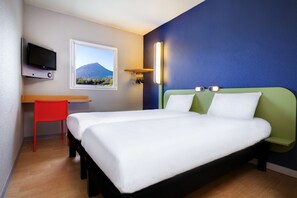Ein Hotelzimmer mit Bett, Schreibtisch, Stuhl, Fernseher und einem Fenster mit Blick auf die Berge.