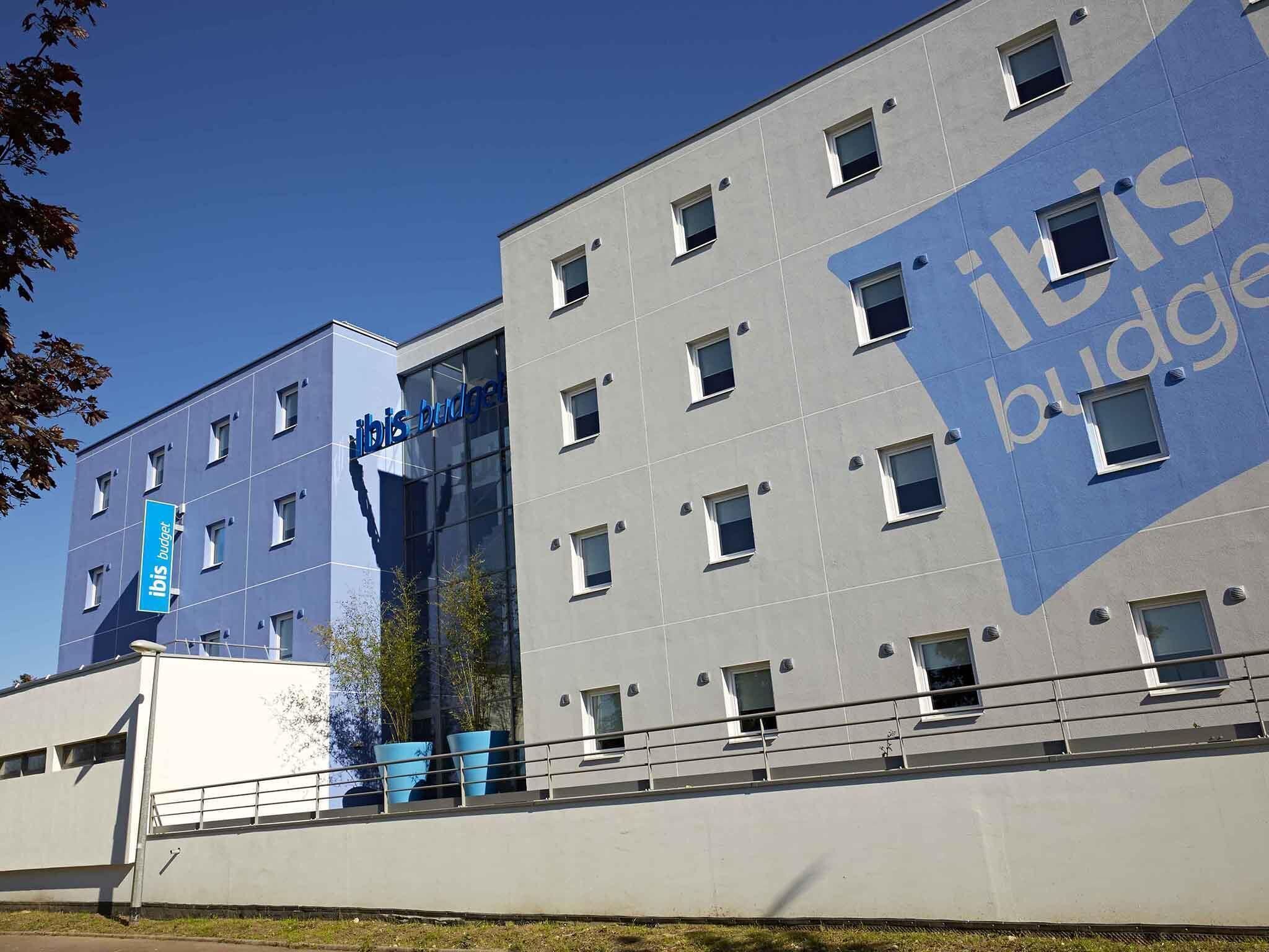 A modern building with the 'ibis budget' logo, multiple windows, and a clear sky.