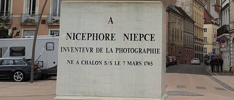 Estátua de Nicephore Niepce segurando uma câmera, com uma placa que diz: "Inventeur de la Photographie" e "Ne a Chalon S/L 7 de Março de 1765".