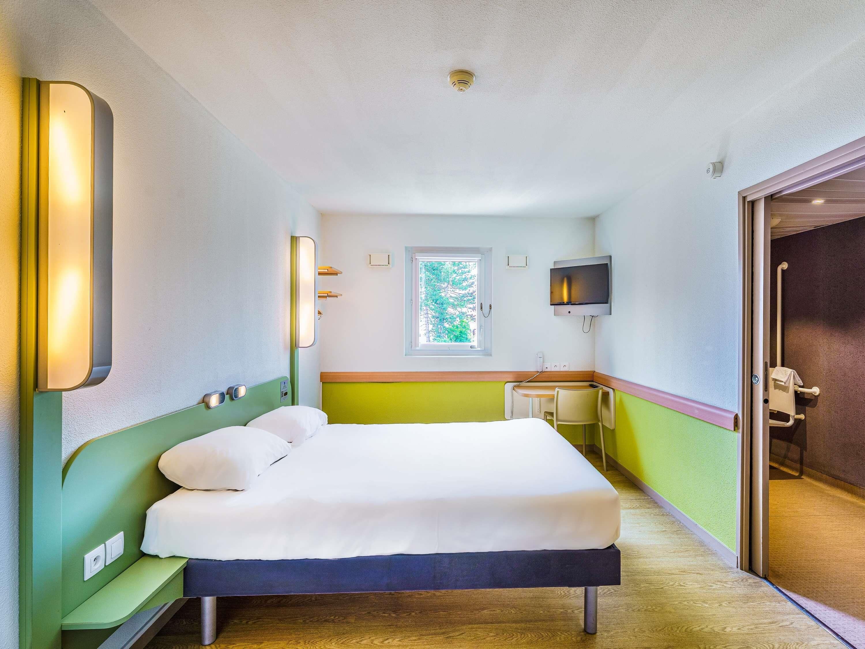 A hotel room with a bed, a desk, a television, a window, and a door.