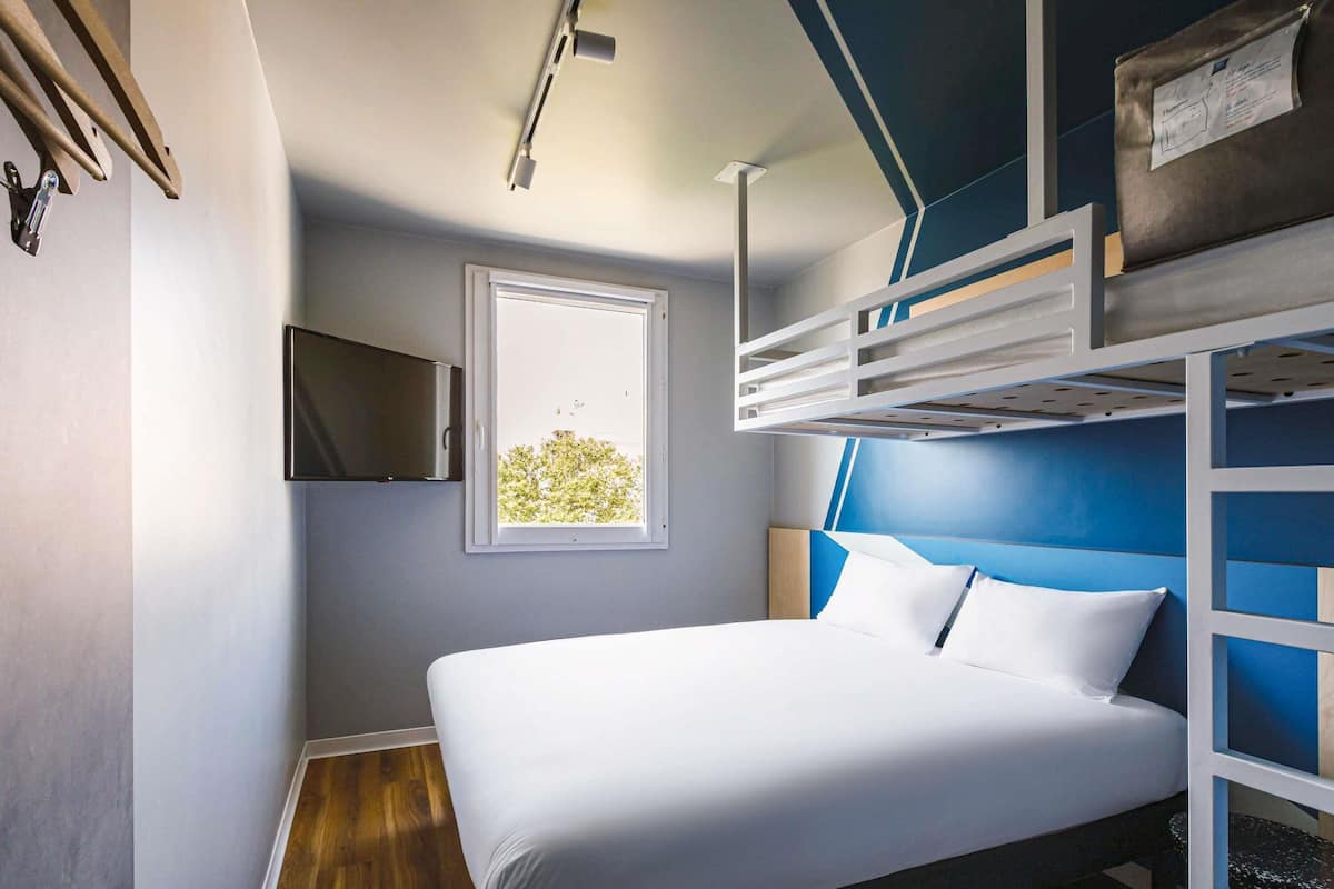 Un dormitorio con literas, una cama individual, una ventana y un televisor montado.