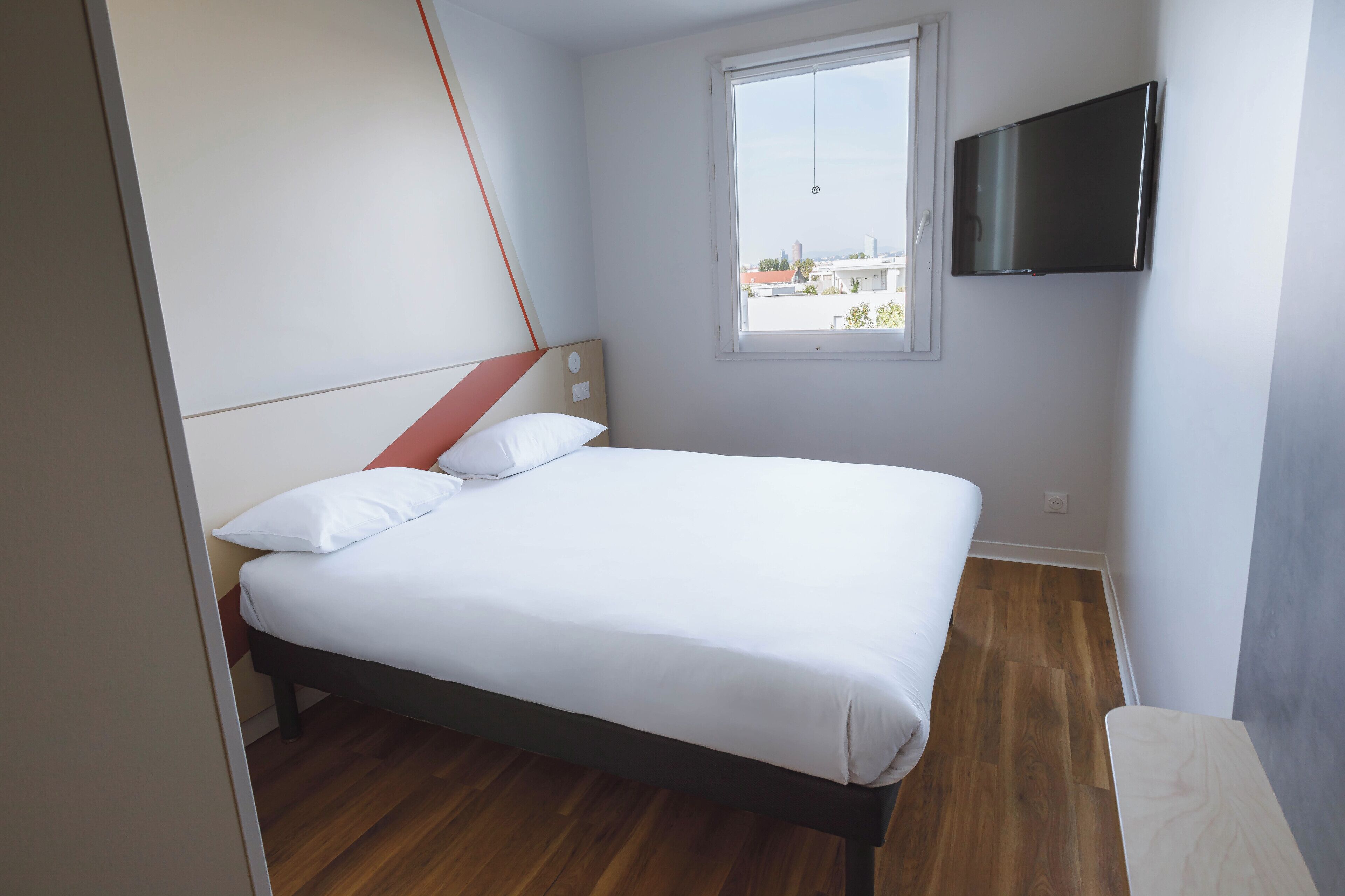 A bedroom with a bed, a window, and a TV mounted on the wall.