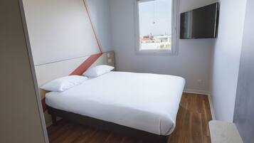 A bedroom with a bed, a window, and a TV mounted on the wall.