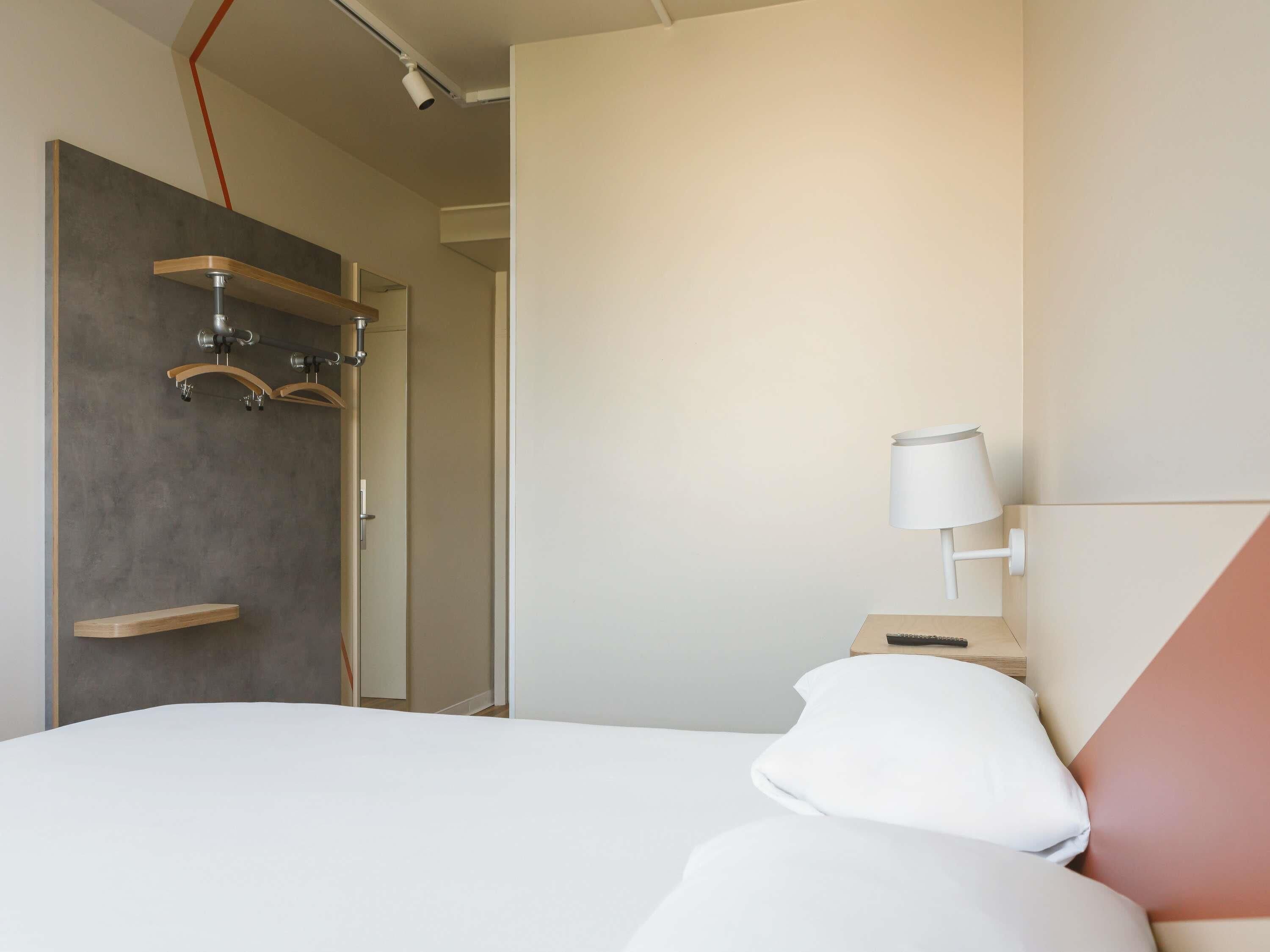 Een hotelkamer met een bed, nachtkastje, lamp, kledingkast en een deur.
