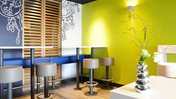 A modern bar area with wooden slatted blinds, a vibrant green wall, and a white counter with a decorative vase.