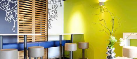 A modern bar area with wooden slatted blinds, a vibrant green wall, and a white counter with a decorative vase.