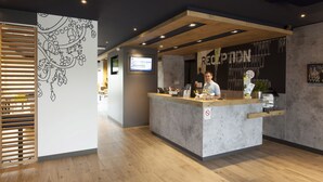 A reception desk with a modern design, a digital screen, and a wall with a floral pattern. - ibis budget Cherbourg La Glacerie (Cherbourg-en-Cotentin)