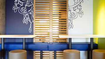 Una zona de estar con un banco y taburetes, una pared con un diseño decorativo y una ventana con persianas.