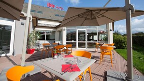 An outdoor patio area with tables and chairs, a large umbrella, and a sign for 'Ibis Hotel'. - ibis budget Cherbourg La Glacerie (Cherbourg-en-Cotentin)