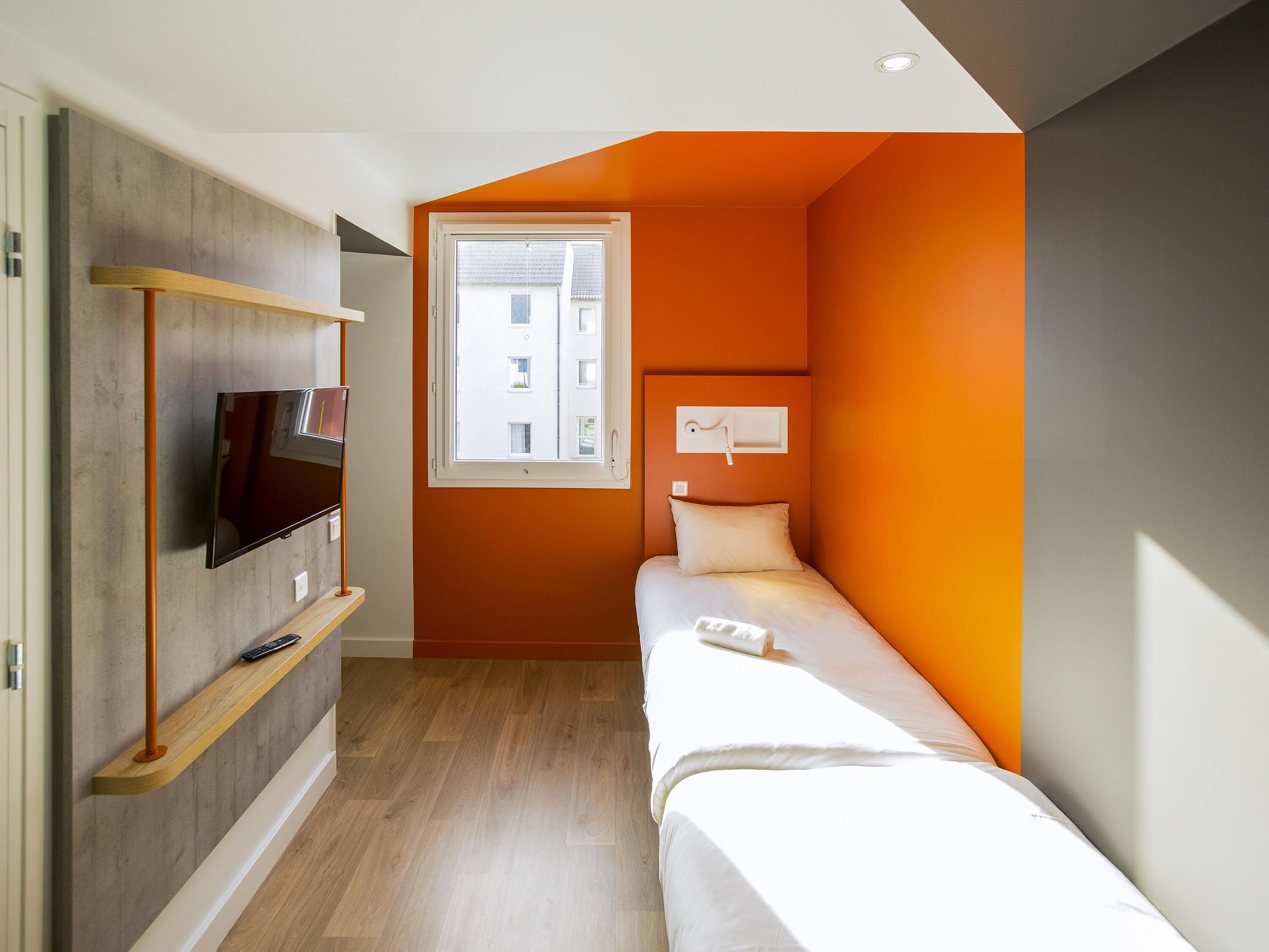 Un dormitorio moderno con una cama, un televisor montado en la pared, una ventana y un estante empotrado.