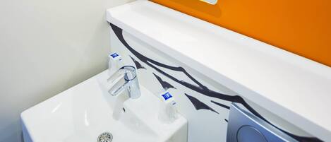 Un baño moderno con un lavamanos blanco, un espejo y un panel decorativo en la pared.