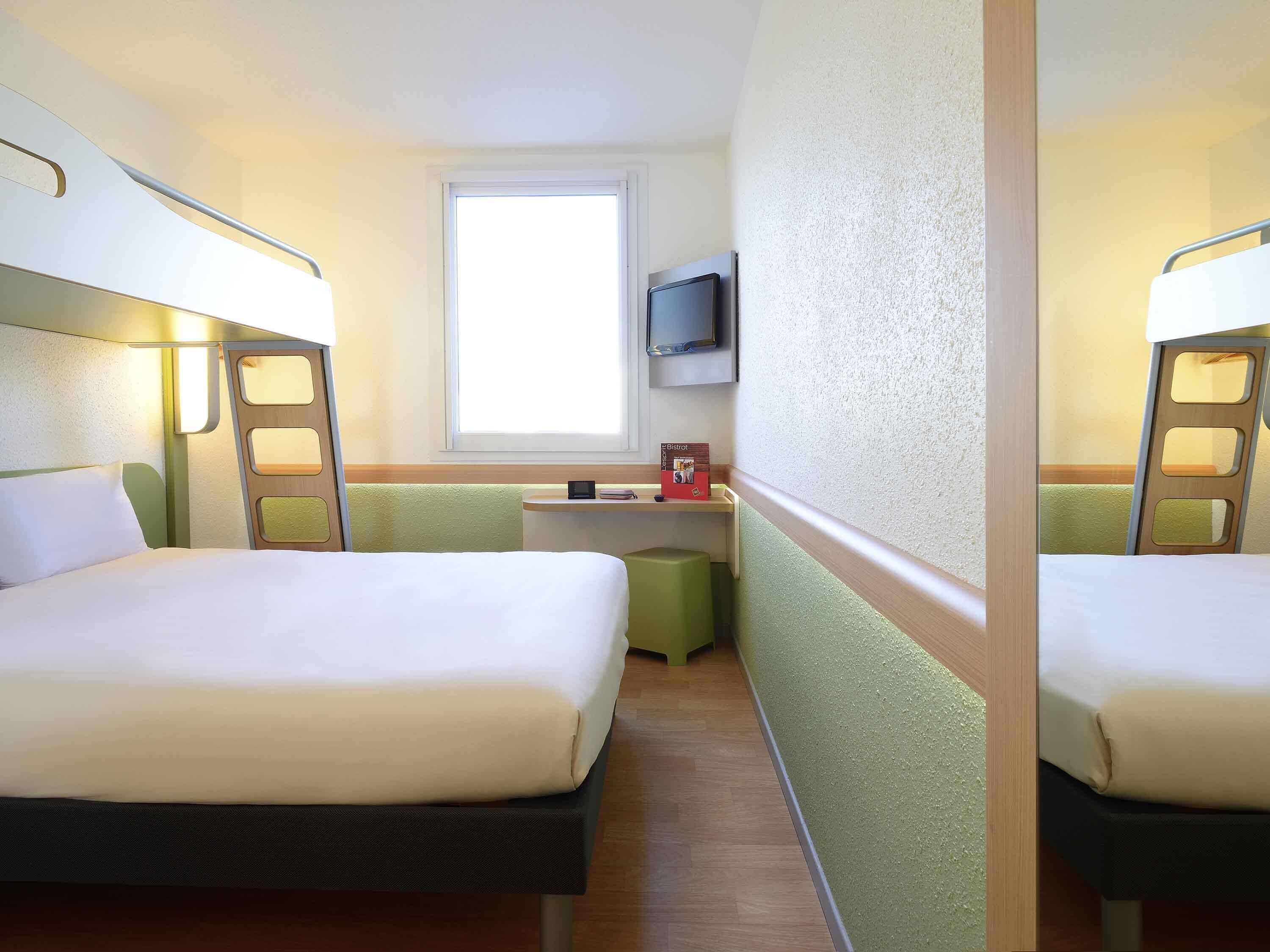 Habitación de hotel con dos camas, un escritorio pequeño, un televisor y una ventana.