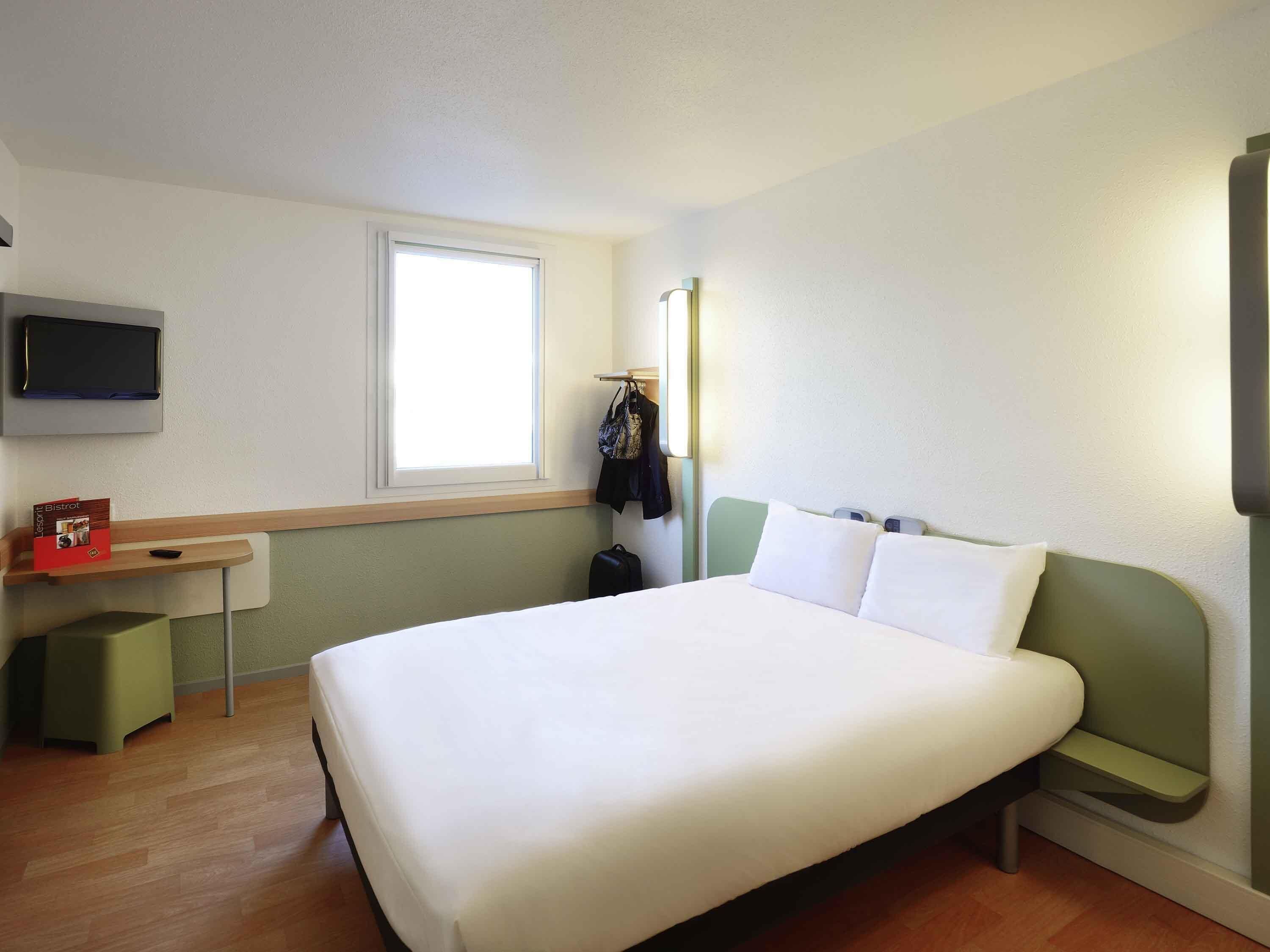 Une chambre d’hôtel équipée d’un lit, d’un bureau, d’une chaise, d’un téléviseur fixé au mur et d’une fenêtre.