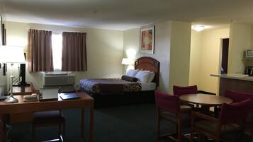 A hotel room with a bed, a desk with a chair, a dining table with chairs, and a television.