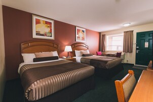 A hotel room with two beds, a desk, a chair, a window with curtains, and artwork on the walls.