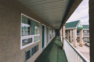 A hotel corridor with multiple rooms, a green carpeted walkway, and a visible balcony railing.