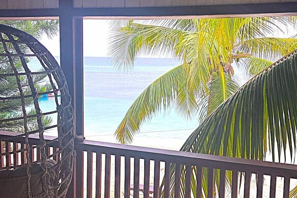 A covered outdoor area with a view of the ocean, a hammock, and a tiled floor.