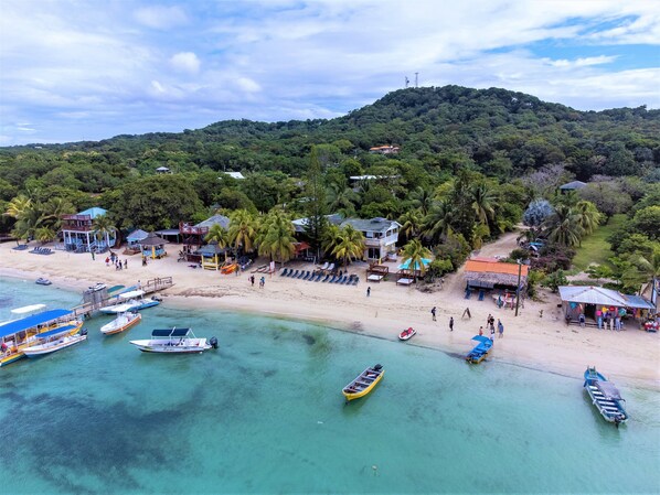 A beach with clear turquoise waters, boats, and a small building with a red roof. - Coconut Tree West Bay (Roatan)