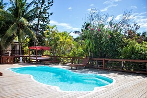 A wooden deck with a swimming pool, surrounded by lush greenery and a wooden fence. - Coconut Tree West Bay (Roatan)