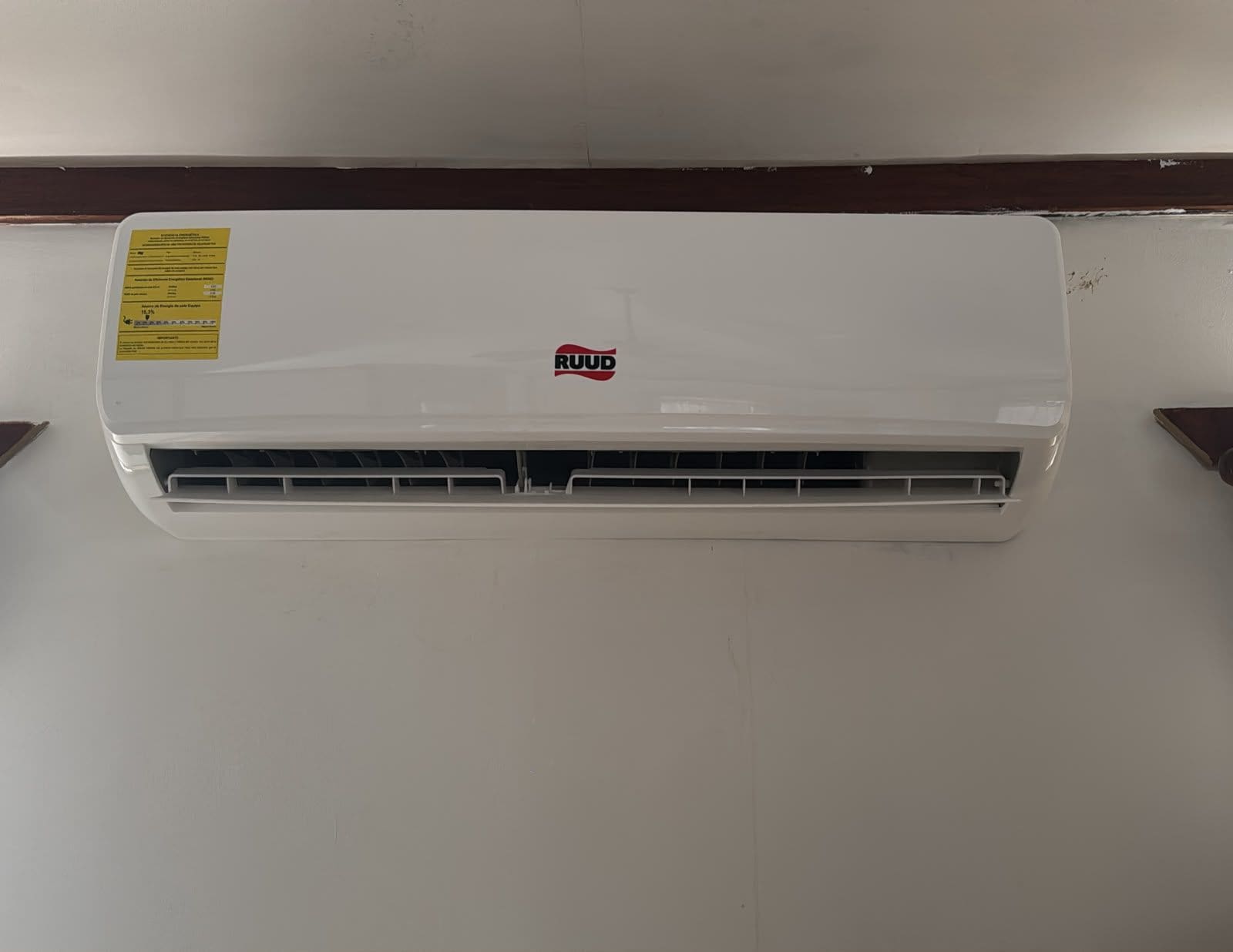 Un equipo de aire acondicionado blanco con una etiqueta amarilla y el nombre de marca 'RUUD'.