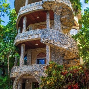 A multi-level stone building with balconies and arched windows, surrounded by lush greenery. - Coconut Tree West Bay (Roatan)