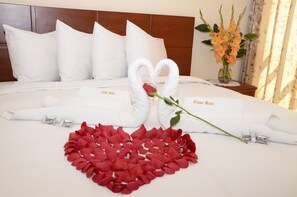 A neatly made bed with white pillows, a heart-shaped arrangement of red rose petals, and two white towels shaped like swans with a red rose between them. - Hoteles Casa Real (Cusco)