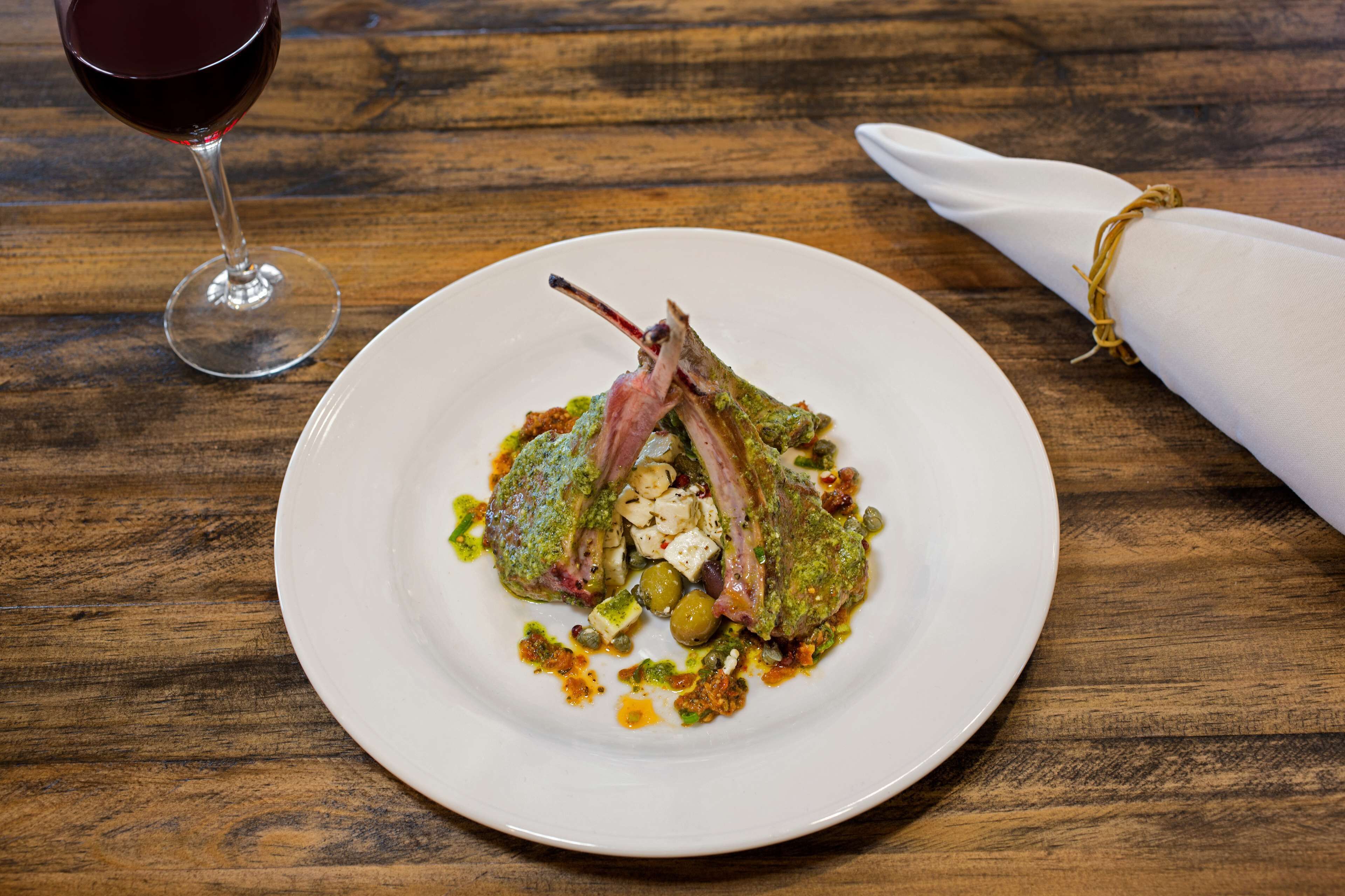 Une assiette de nourriture accompagnée d’un verre de vin rouge, le tout posé sur une table en bois.