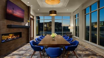 Un comedor moderno con una mesa larga, sillas azules, una chimenea y ventanas amplias con vistas a la ciudad.