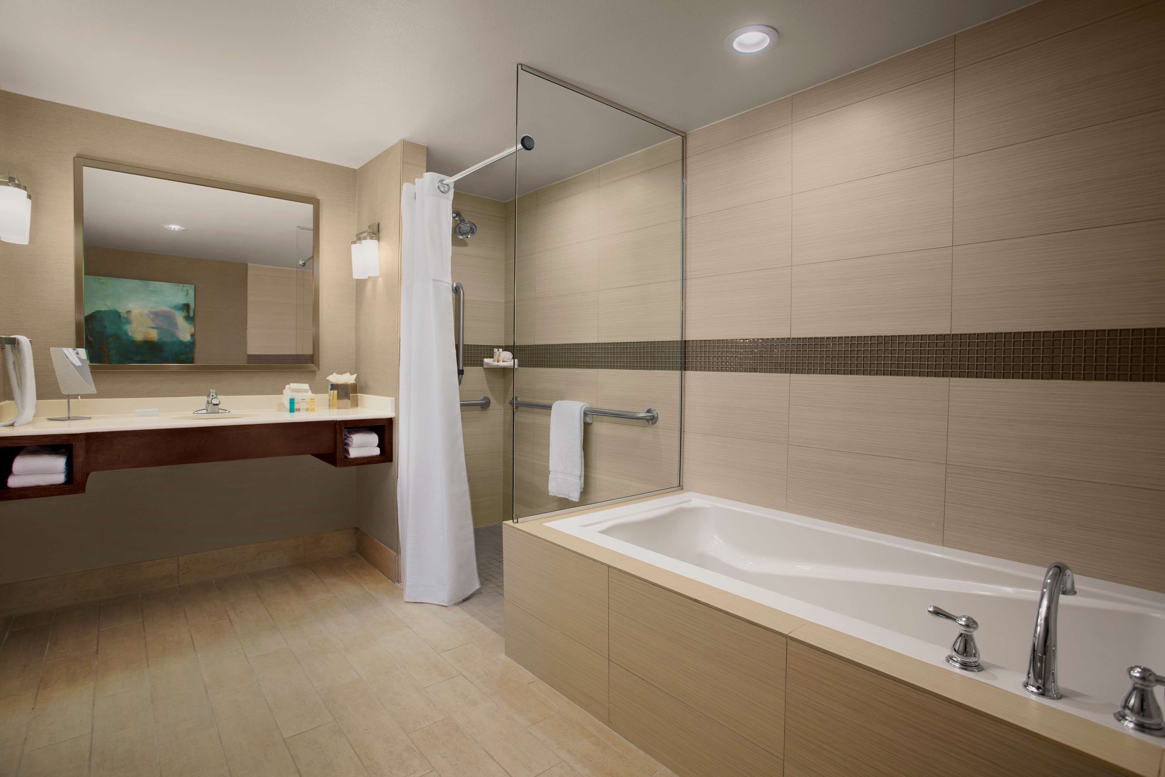 Une salle de bain moderne avec une grande baignoire, une douche à parois de verre, un meuble-lavabo avec un miroir et un porte-serviettes.