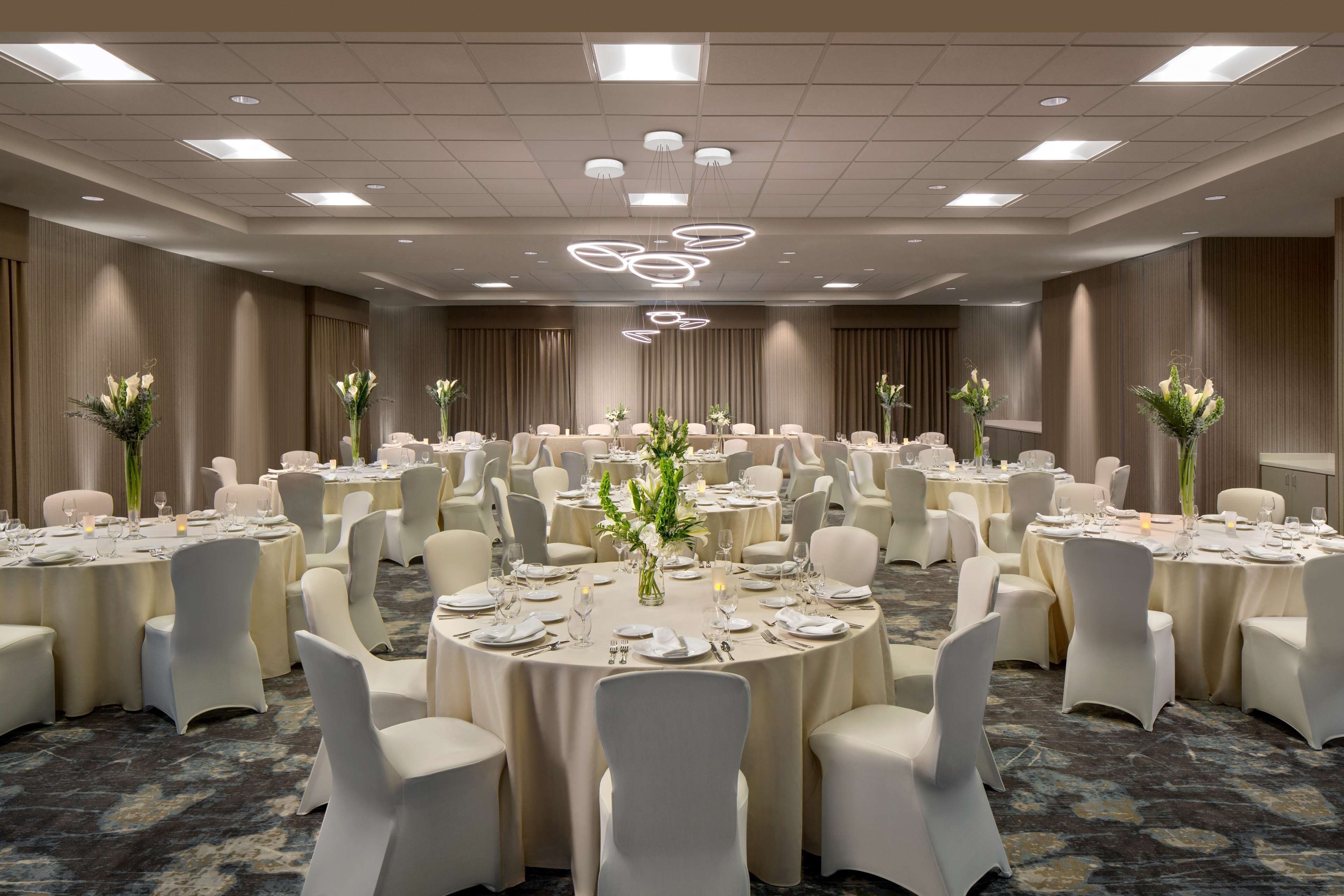 A large banquet hall with round tables, white chairs, and floral centerpieces.