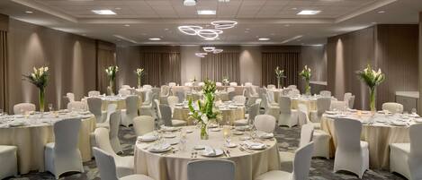A large banquet hall with round tables, white chairs, and floral centerpieces.