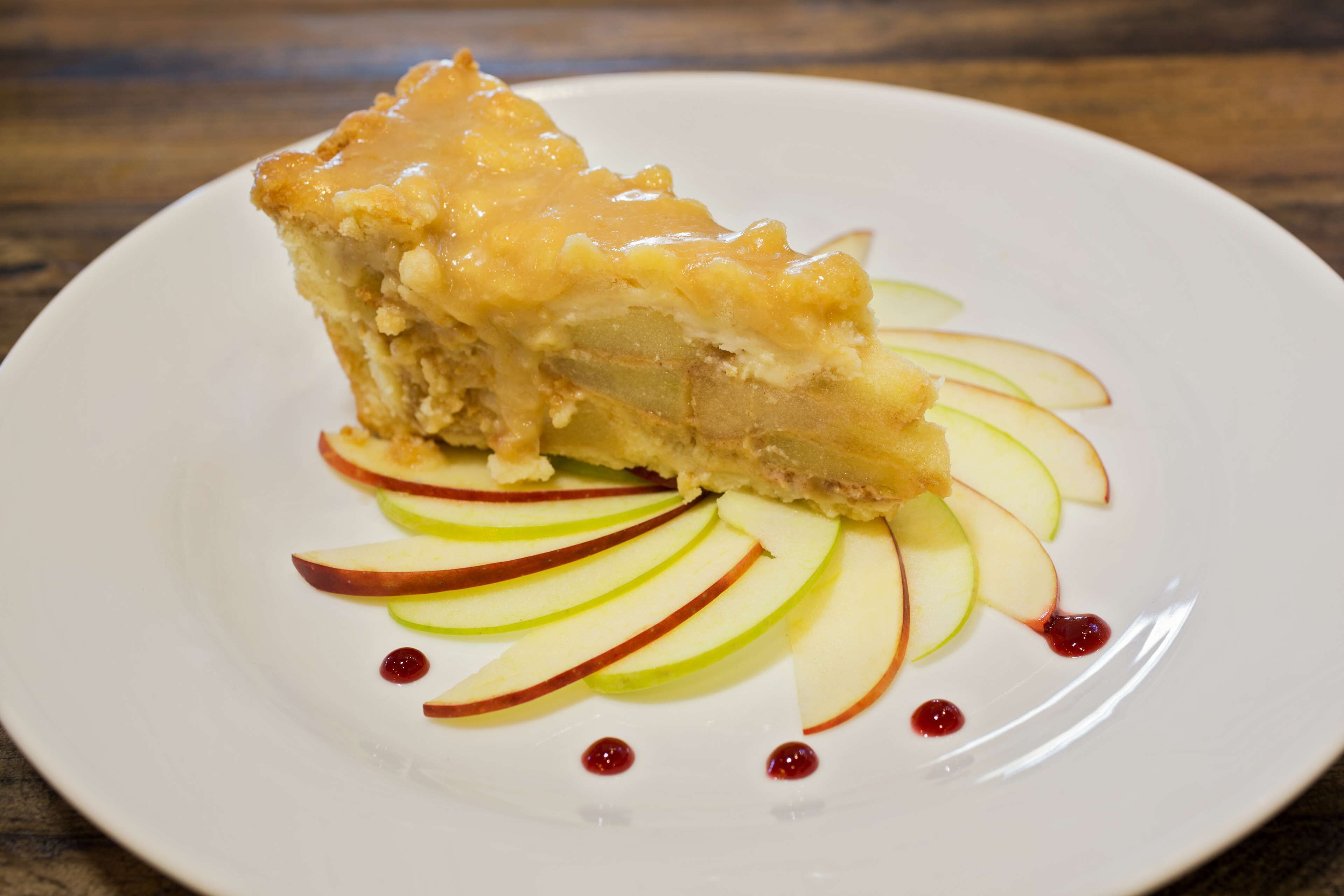 A slice of pie with apple slices and a drizzle of sauce on a plate.