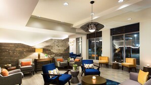 Un espace de détente moderne doté de nombreux sièges, notamment des canapés et des fauteuils, disposés autour d’une table basse centrale. Un mur en pierre et de grandes fenêtres offrent une vue sur l’extérieur.