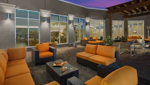 Un espace extérieur aménagé en terrasse, avec des sièges orange, de grandes fenêtres et une structure en forme de pergola.