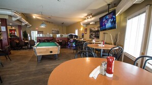 Una mesa de billar, una mesa de pool y un televisor montado en la pared.