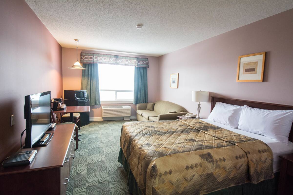 A hotel room with a bed, desk, chair, television, and a window with curtains.