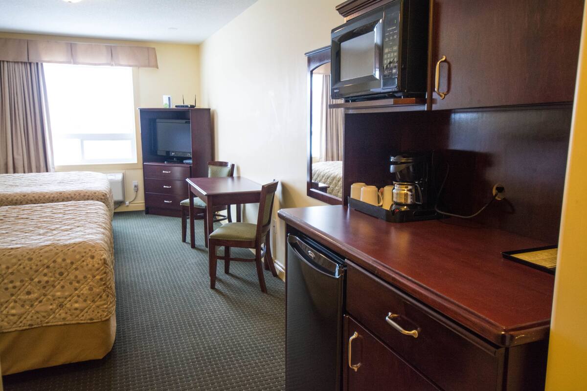 A hotel room with two beds, a dining table, a microwave, a coffee maker, and a television.