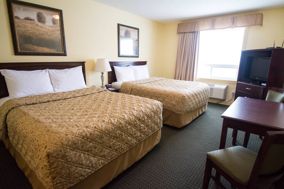 A hotel room with two beds, a desk, a chair, a television, and a window with curtains.