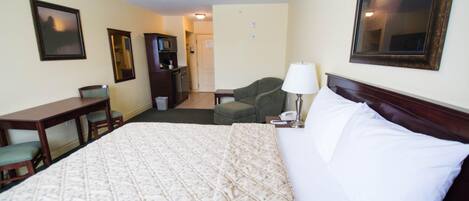 A hotel room with a large bed, a desk, a chair, a lamp, and a TV.