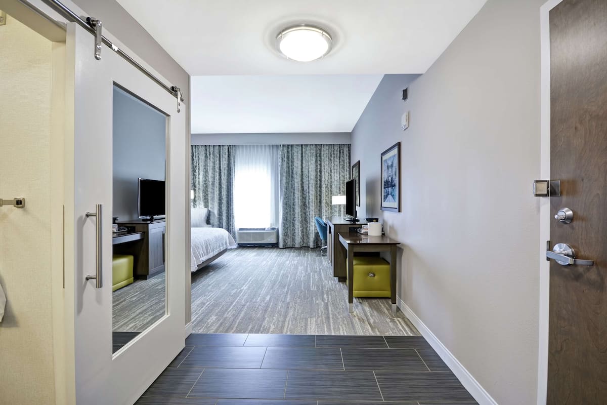 A hotel room with a bed, a desk, a chair, a television, and a window with curtains.
